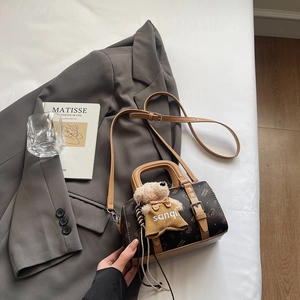 Detail der Boston Bag mit Monogramm-Muster und Bärenanhänger auf grauem Blazer
