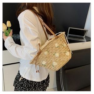 Close-up of straw tote bag with daisy embroidery and brown leather shoulder straps