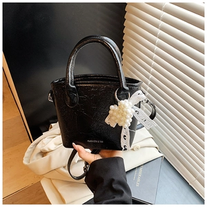 Détail d'un sac seau noir brillant à texture froissée avec perles et nœud en dentelle