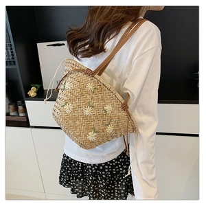 Detail view of woven straw tote bag featuring white daisy embroidery and drawstring closure