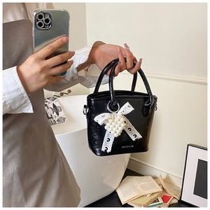 Dettaglio di una mini borsa a secchiello nera con ciondolo a cuore di perle e finitura lucida