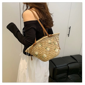 Detail of straw tote bag featuring white daisy embroidery and brown leather shoulder straps