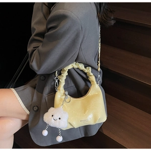 Detail of pleated beige cloud bag with silver chain strap and plush pendant