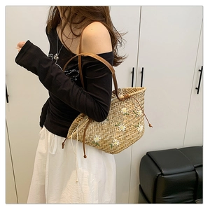 Detail of woven straw tote bag featuring white daisy embroidery and brown leather strap