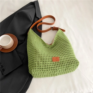 Close-up of green woven tote bag with brown leather strap and logo detail on white fabric