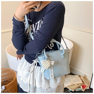 Dettaglio della mini borsa a secchiello azzurra con pizzo bianco e ciondolo a cuore