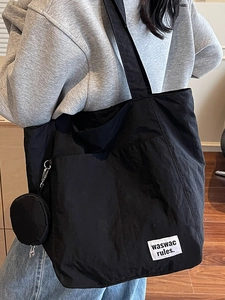 Large black nylon tote bag with small round coin purse shown on a model in a casual setting