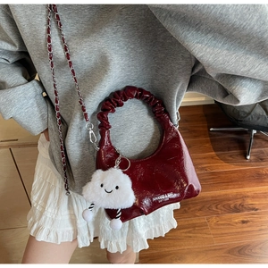 Detail view of burgundy pleated handbag with ring handle and white cloud plush charm