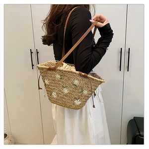Detail of straw tote bag featuring white daisy embroidery and brown leather shoulder straps