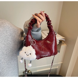 Close-up of wine red pleated handbag with glossy finish, chain strap and cloud charm