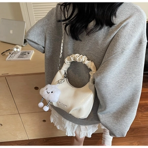 Close-up of cream pleated cloud bag with silver chain and cute plush charm on a wooden desk