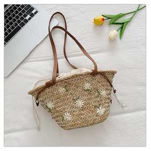 Detail of straw tote bag with daisy embroidery, leather handles and drawstring liner