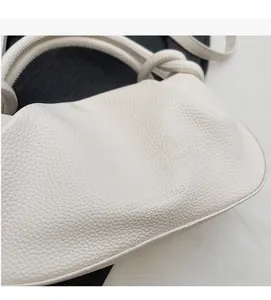 Detail of white lychee leather texture and debossed logo on the pleated bucket bag