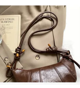 Detail of a brown glossy croissant shoulder bag featuring unique knotted strap with gold tips