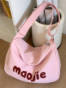 Pink canvas hobo shoulder bag with logo print and adjustable strap on wood floor