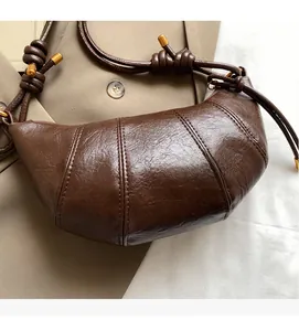 Detail of a brown pleated leather croissant bag with knotted strap and metal end caps