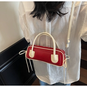 Detail view of stylish red shoulder bag with white trim and decorative side ribbons