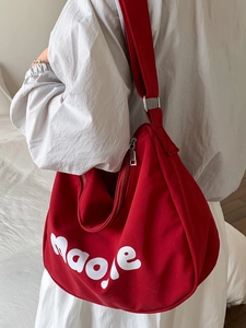 Red canvas tote bag with white letter print and adjustable strap worn on white shirt