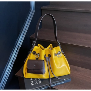 Detail of yellow bucket bag with brown drawstrings and a mini pouch on wooden stairs