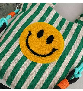 Détail du sac cabas à rayures vertes avec patch smiley jaune et anse en corde tressée
