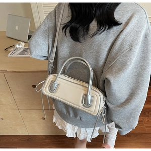 Detail of a chic cream and silver underarm bag with metallic handles and elegant side tassels