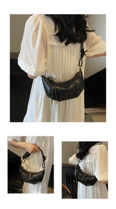 Detail of black leather croissant bag with knotted strap and gold metal hardware