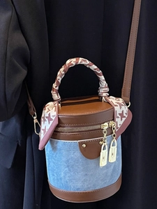Denim bucket bag with brown leather trim and scarf-wrapped handle on dark background