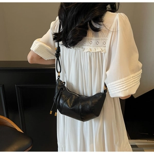 Detail of a black crescent crossbody bag worn by a model in a white lace dress