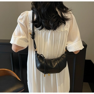Detail of black pleated crescent crossbody bag with minimalist shoulder strap knot