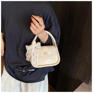 Détail d'un sac à main crème élégant avec un grand nœud en dentelle et boucle dorée
