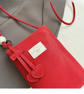 Detail of red PU leather mini phone bag with heart charm, pearl, and white label