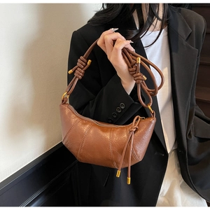 Brown croissant shoulder bag with knotted strap and gold hardware detail on a model