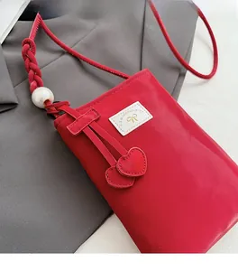 Detail of red nylon phone bag with heart charms, a large pearl, and woven strap