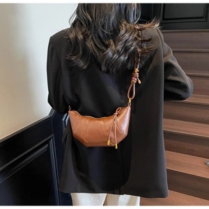 Brown faux leather crescent bag worn crossbody over a black blazer on wooden stairs