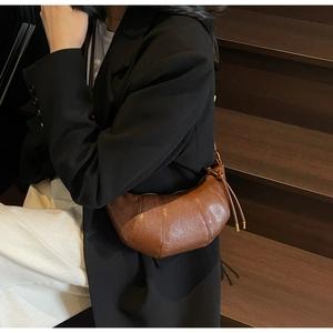 Brown croissant shoulder bag with drawstring detail worn by a model in a minimal setting