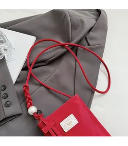 Detail of red glossy crossbody phone bag with pearl strap accents on grey blazer