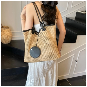 Straw woven tote bag with black handles on white dress model for beach vacation styling