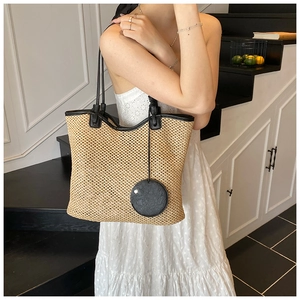 Detailed texture of hand-woven straw tote bag with black leather straps and charm
