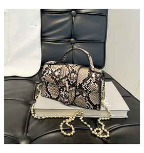 Close-up of snakeprint handbag featuring a gold bead chain and top handle on a book