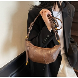 Detail showing brown pleated crescent bag texture with metal tassels and knot strap