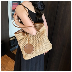 Close-up of a large straw tote bag with brown leather handles and a round pendant detail