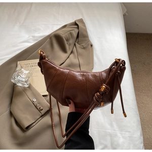 Detail of a dark brown leather croissant bag with knotted strap and gold metal accents