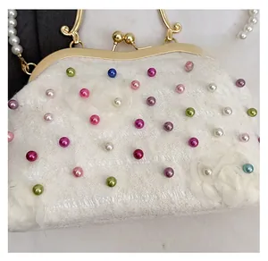 Dettaglio borsa a conchiglia in pizzo bianco con perle colorate e finiture dorate