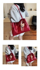 Detail view of red crocodile pattern tote bag featuring a cute teddy bear charm accessory