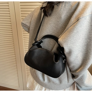 Detail of black lychee grain leather crossbody cloud bag with knot handle on grey sweatshirt