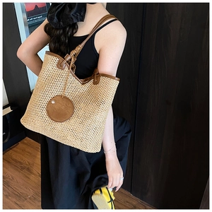 Close-up of woven straw tote bag with brown leather handles and hollow mesh pattern
