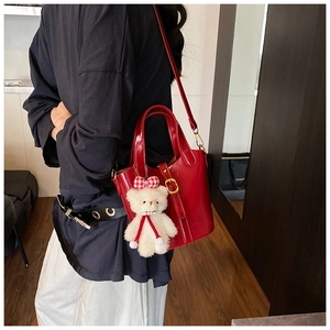 Dettaglio di una borsa a secchiello in pelle lucida rossa con ciondolo a forma di orsetto