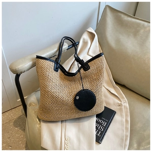Detail shot of the woven straw texture and black leather handles on a large tote bag