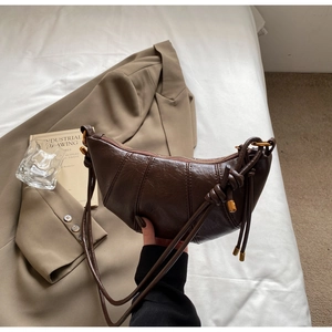 Detail of dark brown croissant bag featuring pleated synthetic leather and knotted shoulder strap