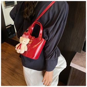 Détail du sac seau en cuir verni rouge avec breloque ours blanc et bandoulière ajustable
